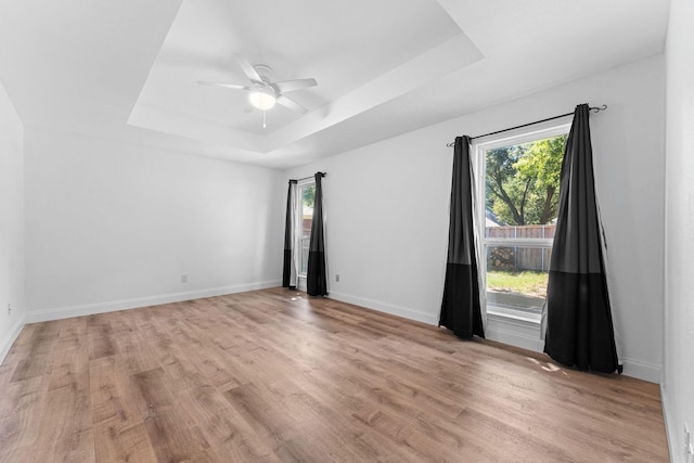 unfurnished room with ceiling fan, light hardwood / wood-style flooring, and a tray ceiling