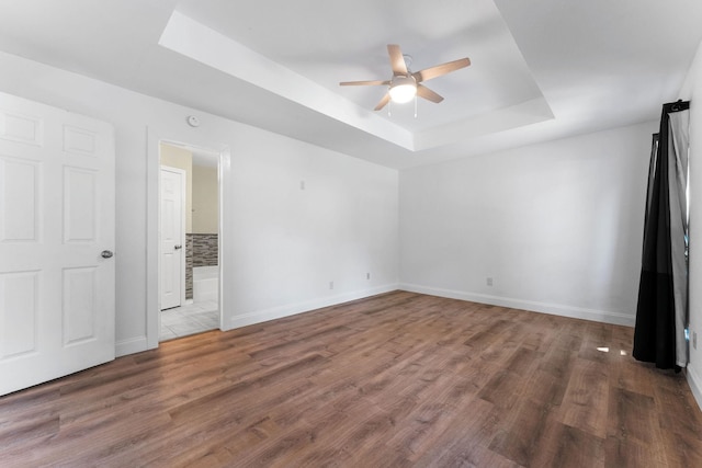 unfurnished bedroom with ceiling fan, a tray ceiling, and dark wood-type flooring