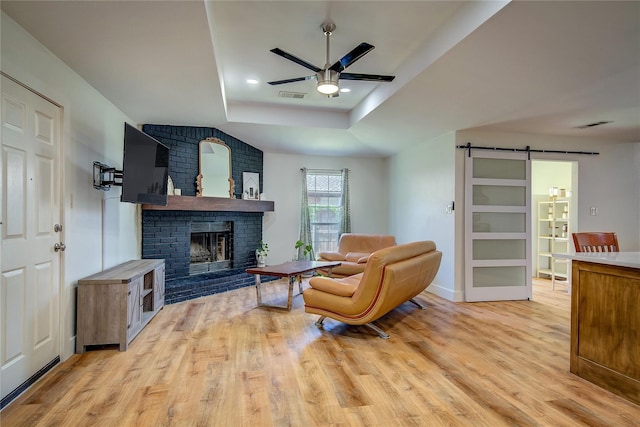 living room featuring a barn door, light hardwood / wood-style flooring, ceiling fan, and a brick fireplace