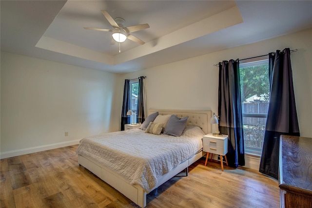 bedroom featuring ceiling fan, a tray ceiling, and light hardwood / wood-style floors