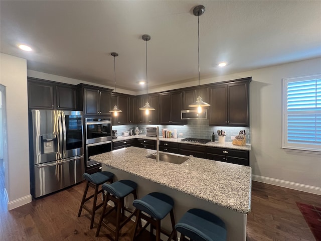 kitchen with pendant lighting, sink, stainless steel appliances, light stone countertops, and a kitchen bar