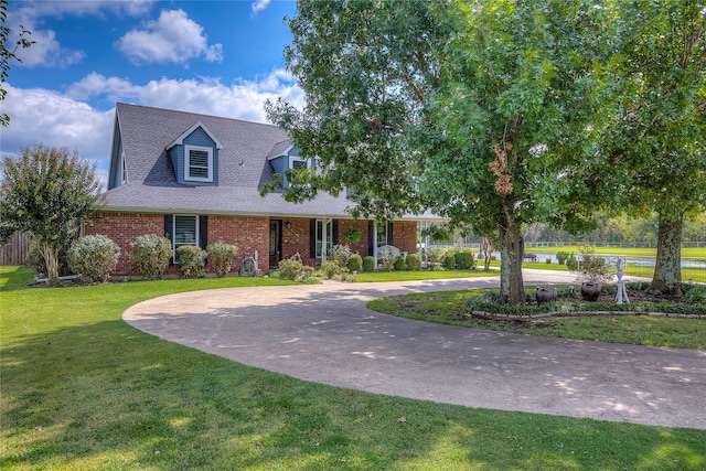 view of front facade featuring a shingled roof, brick siding, curved driveway, and a front lawn