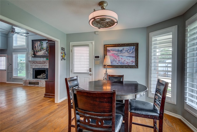 dining room with baseboards, ceiling fan, a fireplace, and light wood-style floors