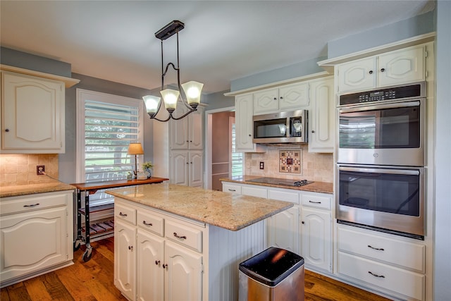 kitchen featuring dark wood-style floors, a kitchen island, light stone countertops, stainless steel appliances, and pendant lighting