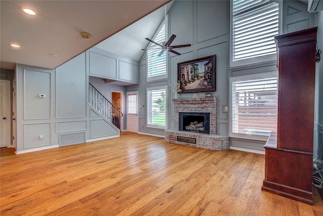 unfurnished living room with a towering ceiling, a brick fireplace, light wood-type flooring, and ceiling fan