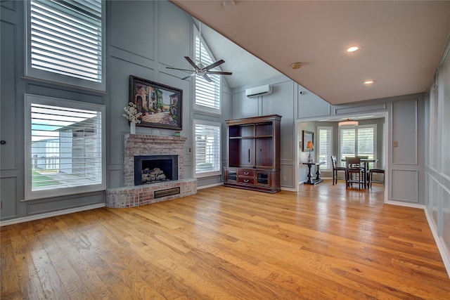 unfurnished living room featuring light hardwood / wood-style floors, a wall unit AC, a fireplace, high vaulted ceiling, and ceiling fan