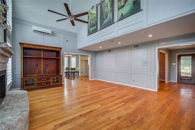 living room with a brick fireplace, light hardwood / wood-style floors, ceiling fan, a wall unit AC, and high vaulted ceiling