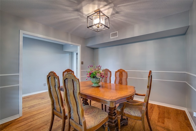 dining area with a chandelier, a textured ceiling, and light hardwood / wood-style floors