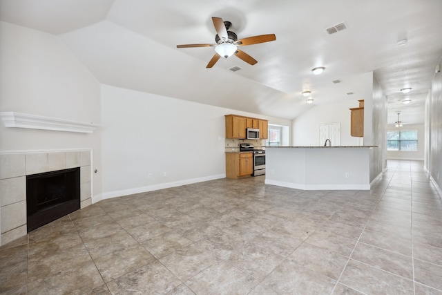 unfurnished living room with ceiling fan, light tile patterned flooring, sink, a tile fireplace, and vaulted ceiling