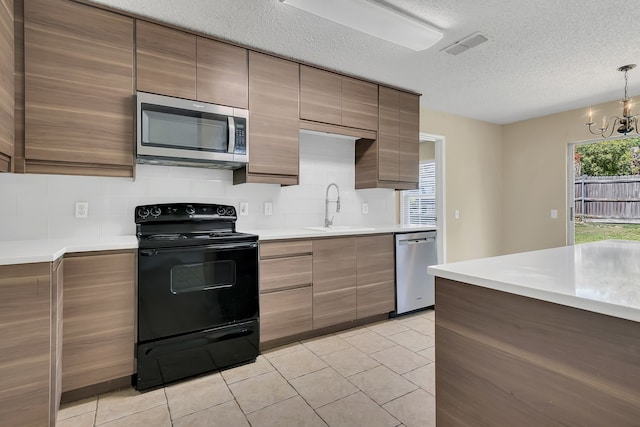 kitchen with pendant lighting, sink, a textured ceiling, stainless steel appliances, and an inviting chandelier