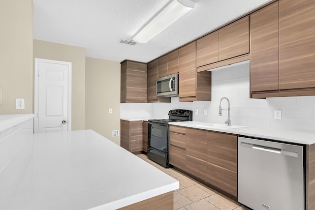 kitchen featuring a textured ceiling, light tile patterned flooring, sink, backsplash, and appliances with stainless steel finishes