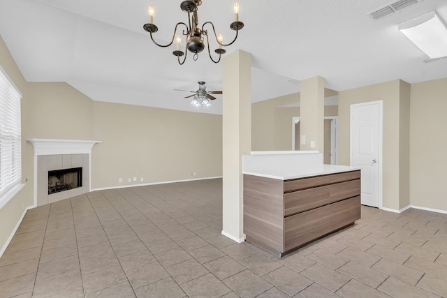 kitchen featuring vaulted ceiling, ceiling fan with notable chandelier, a tiled fireplace, light tile patterned floors, and decorative light fixtures