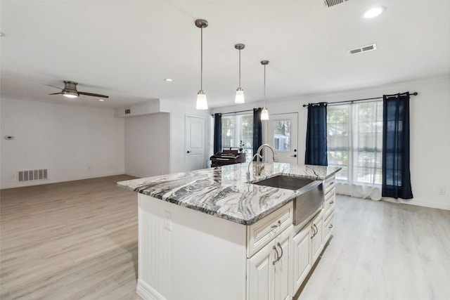 kitchen with a large island, sink, wall chimney range hood, light stone counters, and double oven range