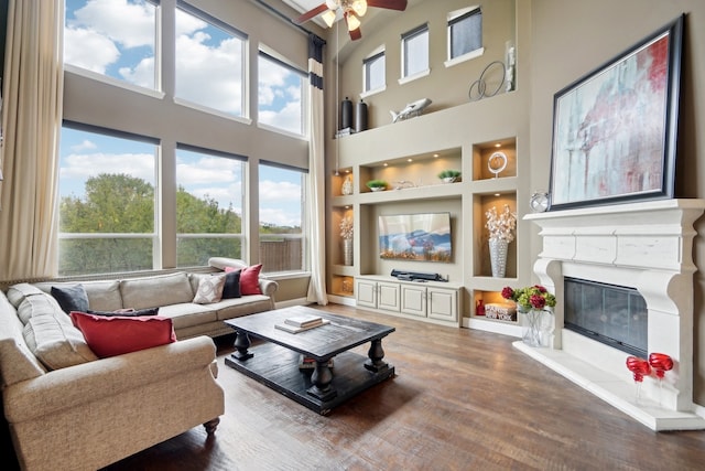 living room featuring ceiling fan, a towering ceiling, hardwood / wood-style floors, and built in shelves