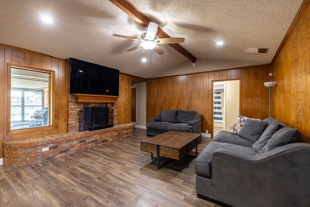 living room featuring ceiling fan, a textured ceiling, a brick fireplace, and hardwood / wood-style floors