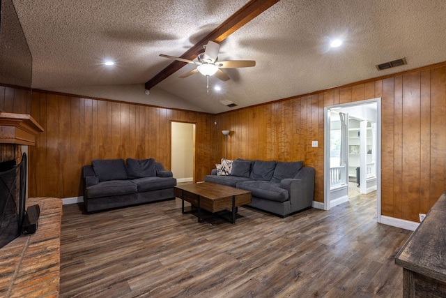 living room with lofted ceiling with beams, dark wood-type flooring, a textured ceiling, ceiling fan, and wooden walls