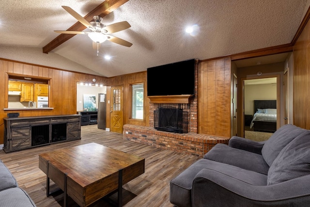 living room with lofted ceiling with beams, a brick fireplace, light hardwood / wood-style floors, and ceiling fan