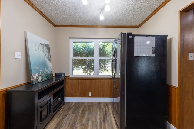 kitchen featuring wood walls, black refrigerator, a textured ceiling, wood-type flooring, and crown molding