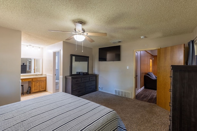 carpeted bedroom featuring ceiling fan, a textured ceiling, ensuite bath, and sink