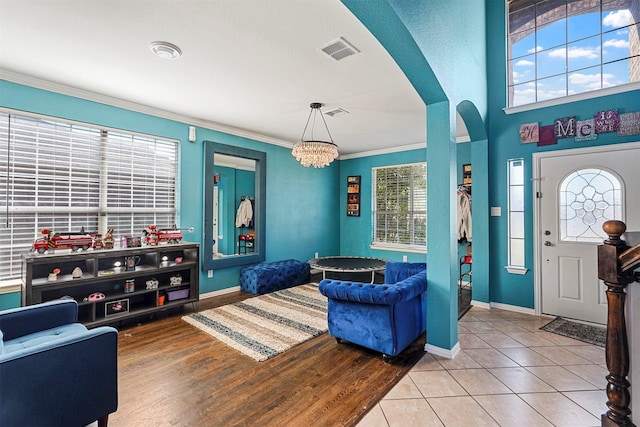 entrance foyer with a chandelier, tile patterned floors, crown molding, and plenty of natural light