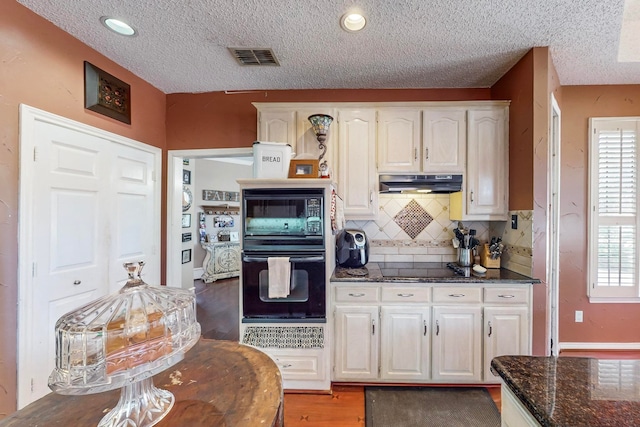 kitchen featuring dark stone counters, white cabinetry, decorative backsplash, black appliances, and dark hardwood / wood-style flooring