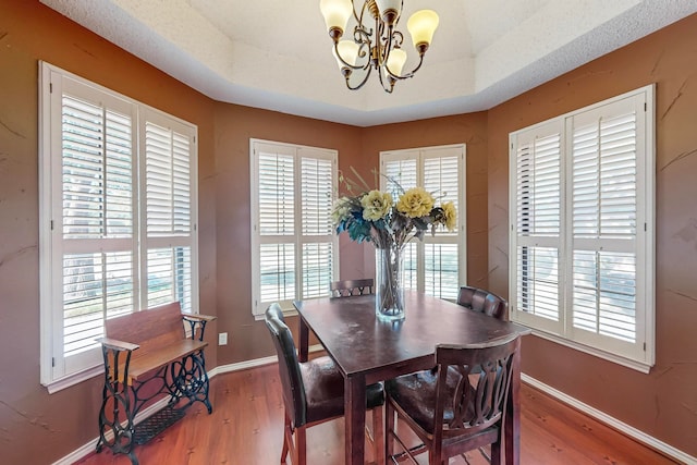 dining space with wood-type flooring, a tray ceiling, an inviting chandelier, and a wealth of natural light