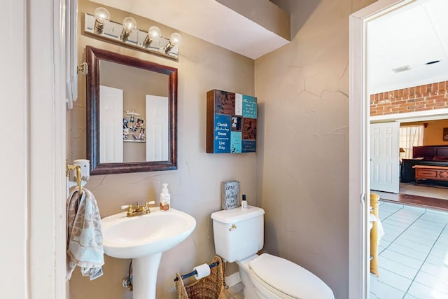 bathroom featuring brick wall, tile patterned flooring, and toilet