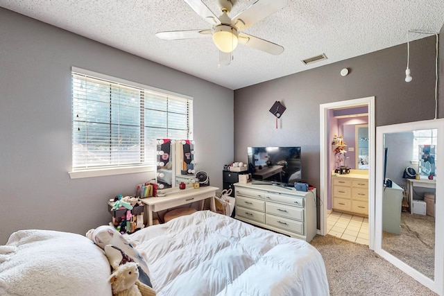 bedroom featuring a textured ceiling, ensuite bath, ceiling fan, and light colored carpet