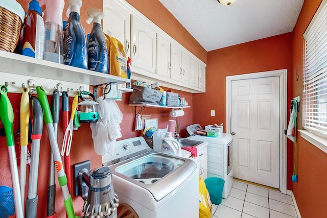 laundry room featuring a textured ceiling, light tile patterned floors, washing machine and clothes dryer, and cabinets