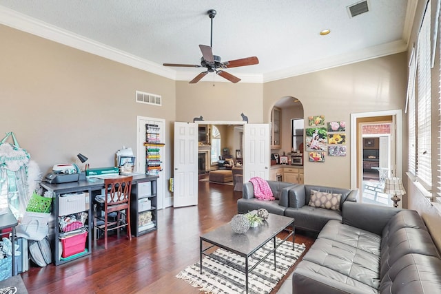 living room with a fireplace, a textured ceiling, ceiling fan, ornamental molding, and dark hardwood / wood-style floors