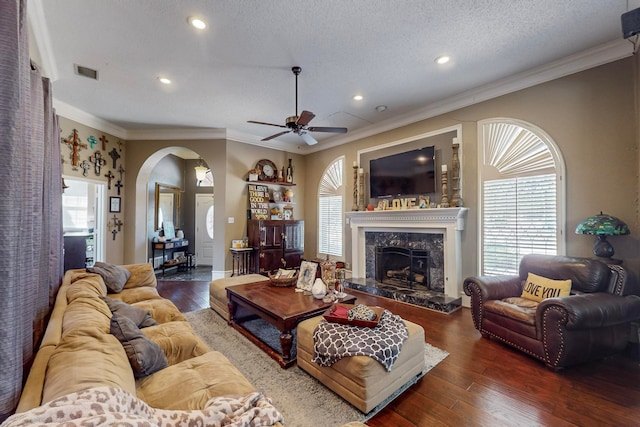 living room with dark wood-type flooring, a fireplace, a textured ceiling, ceiling fan, and ornamental molding