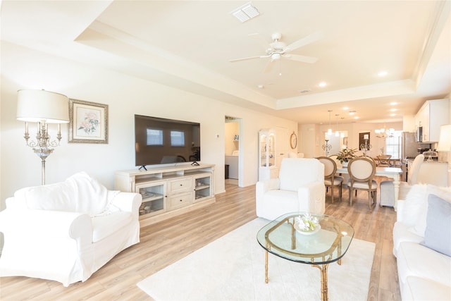 living room with ceiling fan with notable chandelier, a tray ceiling, light hardwood / wood-style flooring, and ornamental molding