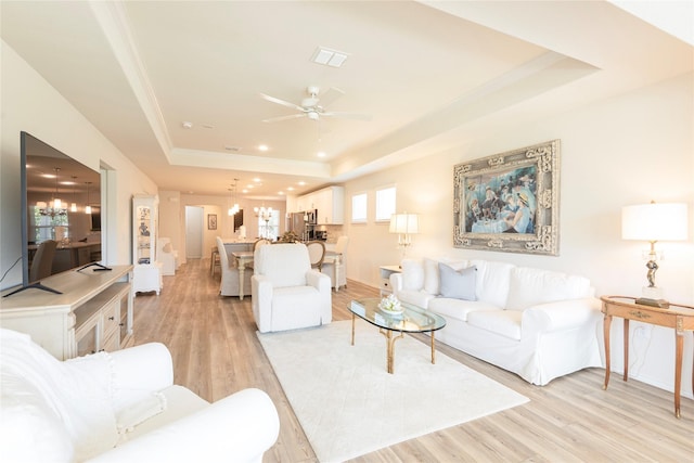 living room featuring ceiling fan with notable chandelier, light hardwood / wood-style flooring, and a tray ceiling