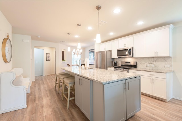 kitchen featuring a center island with sink, decorative light fixtures, white cabinets, and stainless steel appliances