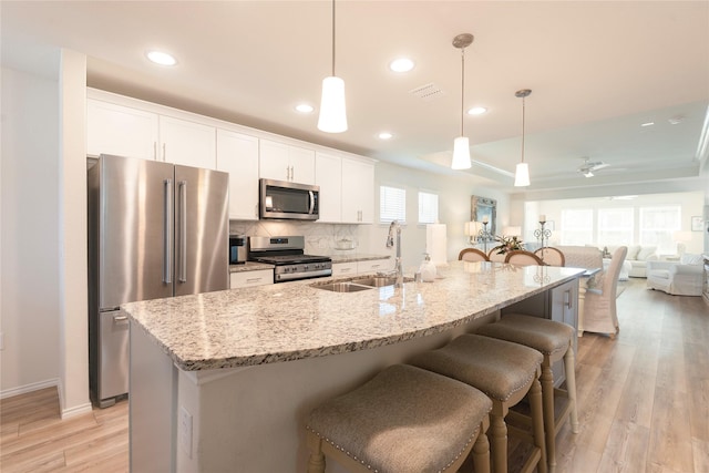 kitchen with hanging light fixtures, stainless steel appliances, a breakfast bar, white cabinets, and a center island with sink