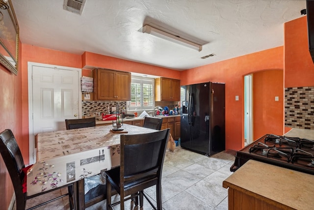 kitchen with a textured ceiling, decorative backsplash, light tile patterned floors, and black fridge