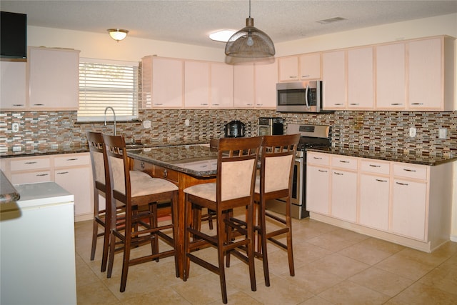 kitchen with dark stone countertops, backsplash, stainless steel appliances, and hanging light fixtures