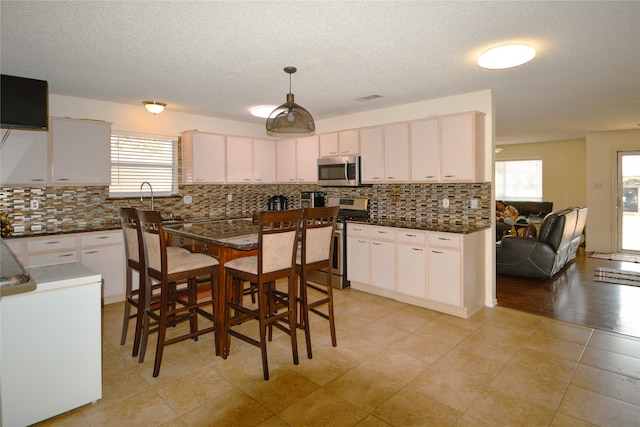 kitchen with pendant lighting, stainless steel appliances, white cabinets, and a wealth of natural light