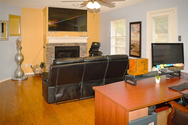 living room featuring ceiling fan, a stone fireplace, and light wood-type flooring