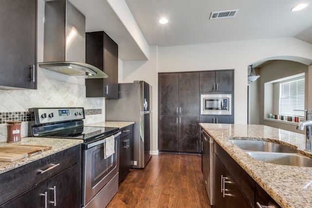 kitchen with light stone counters, sink, wall chimney range hood, stainless steel appliances, and dark hardwood / wood-style flooring