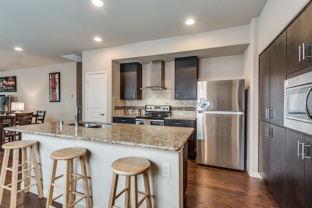 kitchen with dark wood-type flooring, a kitchen island with sink, sink, wall chimney exhaust hood, and stainless steel appliances