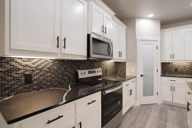 kitchen featuring white cabinets, tasteful backsplash, dark stone counters, light hardwood / wood-style flooring, and stainless steel appliances