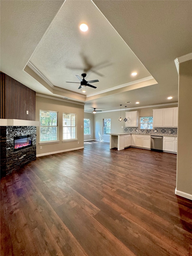 unfurnished living room featuring ceiling fan, a raised ceiling, a textured ceiling, ornamental molding, and dark wood-type flooring