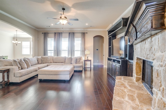 living room with a stone fireplace, ceiling fan with notable chandelier, dark hardwood / wood-style floors, and crown molding