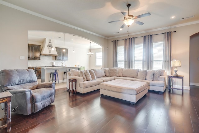 living room with ceiling fan with notable chandelier, crown molding, and dark wood-type flooring