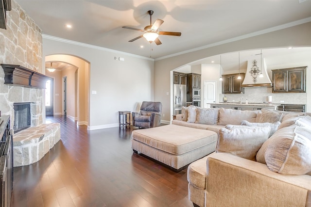 living room with crown molding, a fireplace, dark wood-type flooring, and ceiling fan