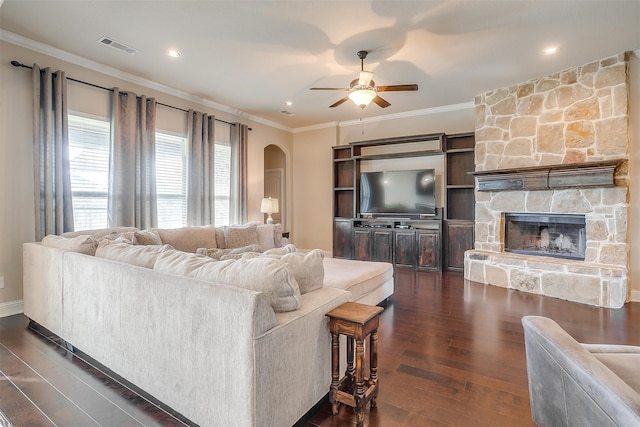 living room with crown molding, a stone fireplace, dark hardwood / wood-style flooring, and ceiling fan