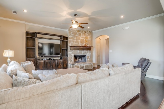 living room featuring ceiling fan, a stone fireplace, crown molding, and dark wood-type flooring