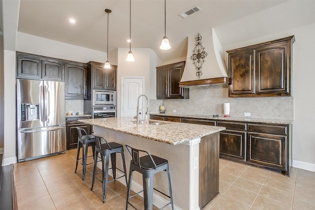 kitchen featuring appliances with stainless steel finishes, a center island with sink, decorative backsplash, and dark brown cabinets