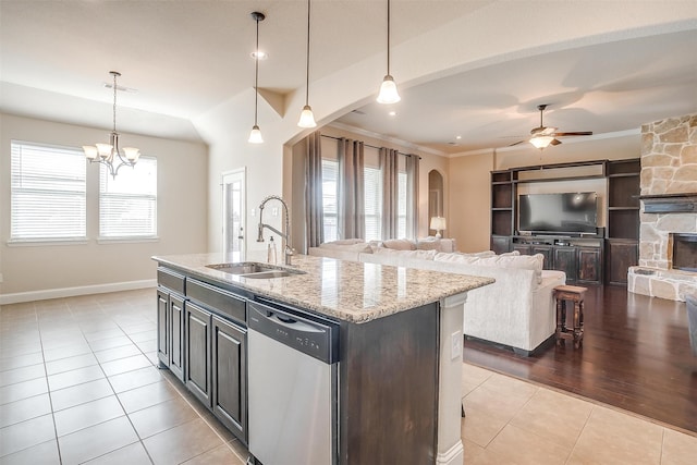 kitchen with a healthy amount of sunlight, a center island with sink, a stone fireplace, and dishwasher